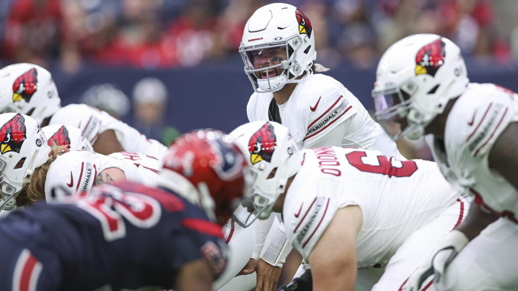 Arizona QB Kyler Murray, in all white, stands behind his offensive line at the line of scrimmage