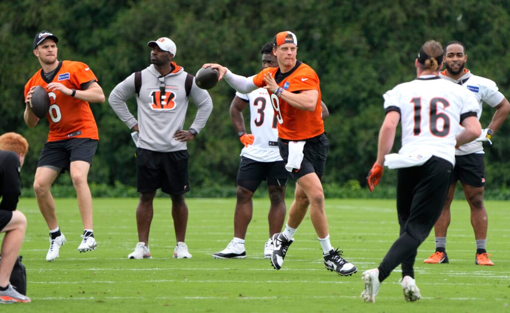 Cincinnati Bengals QB Joe Burrow (orange practice jersey, black shorts, backward orange cap) looks to throw during a practice workout with teammates casually around him