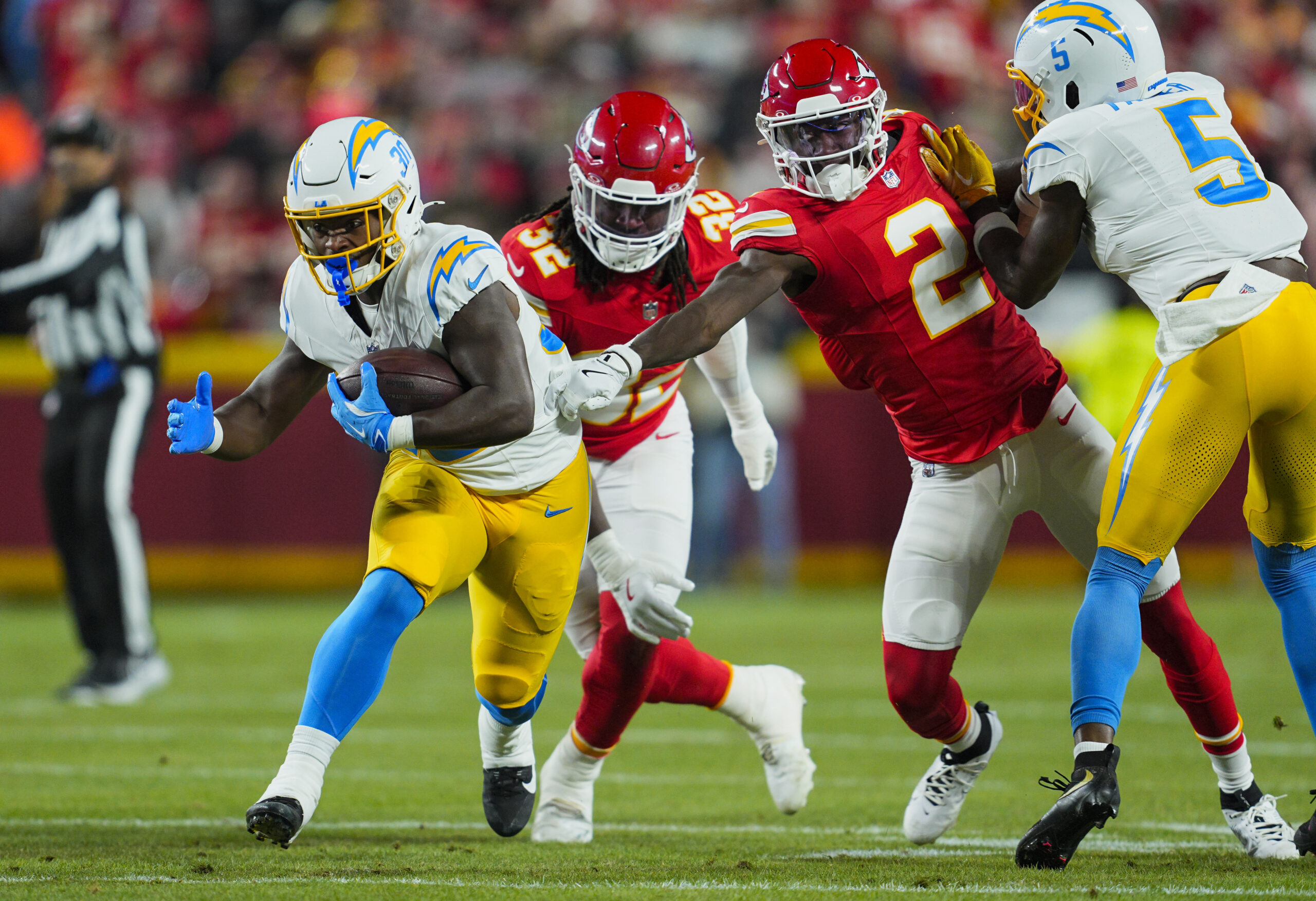 Los Angeles Chargers running back Kimani Vidal (30) runs the ball against Kansas City Chiefs linebacker Nick Bolton (32) and cornerback Joshua Williams (2) during the first half at GEHA Field at Arrowhead Stadium.