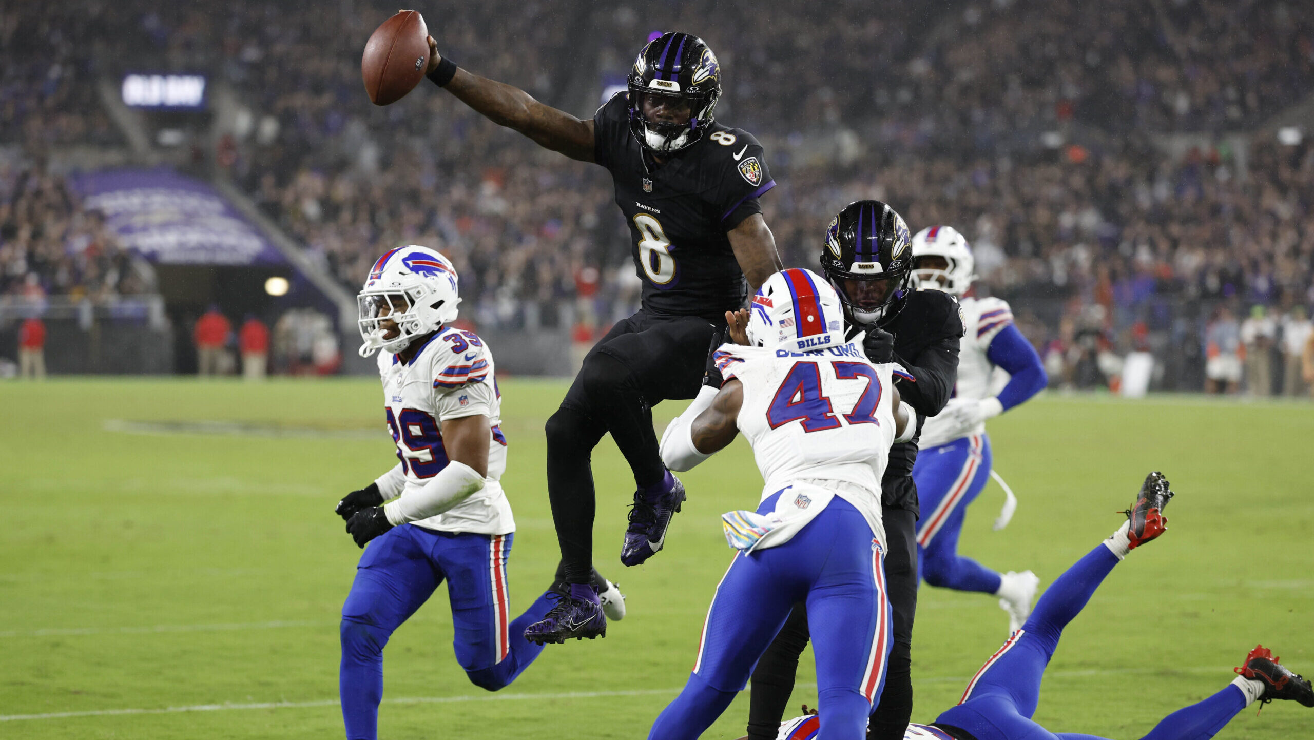 Baltimore Ravens quarterback Lamar Jackson (8) leaps across the goal line for a touchdown as Buffalo Bills Christian Benford (47) and Bills Cam Lewis (39) defend at M&T Bank Stadium.