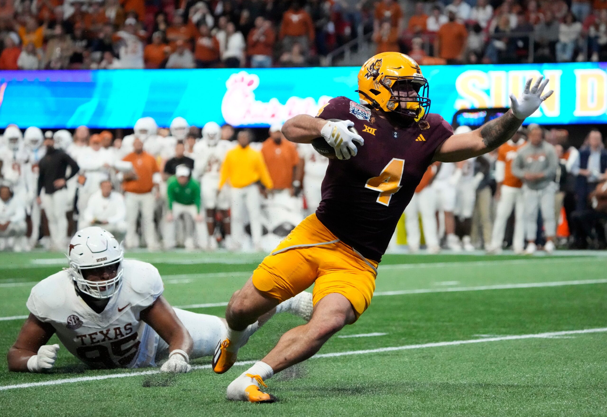 Arizona State running back Cam Skattebo (4) escapes a tackle by Texas defensive lineman Alfred Collins (95) during the fourth quarter in the Chick-fil-A Peach Bowl in Atlanta.